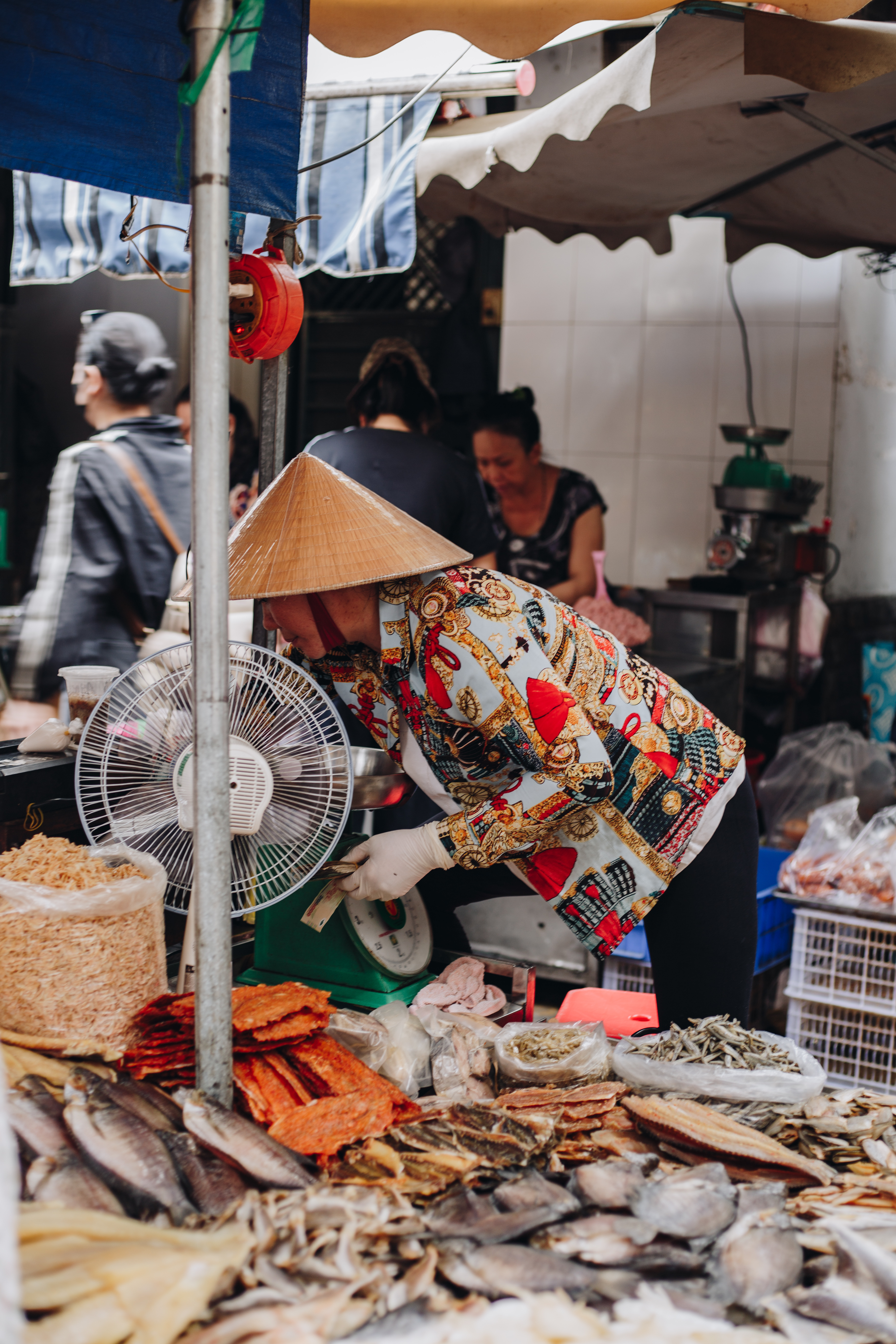 A market vendor in a conical hat at a dried goods stall in Saigon
