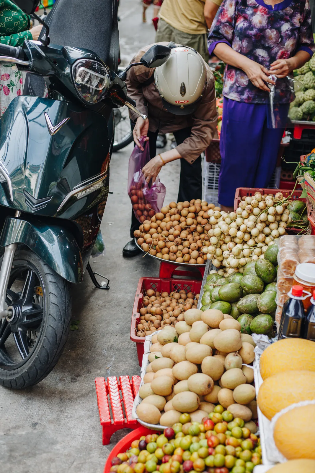 A guest browsing fruit at a market stall next to a parked motorbike