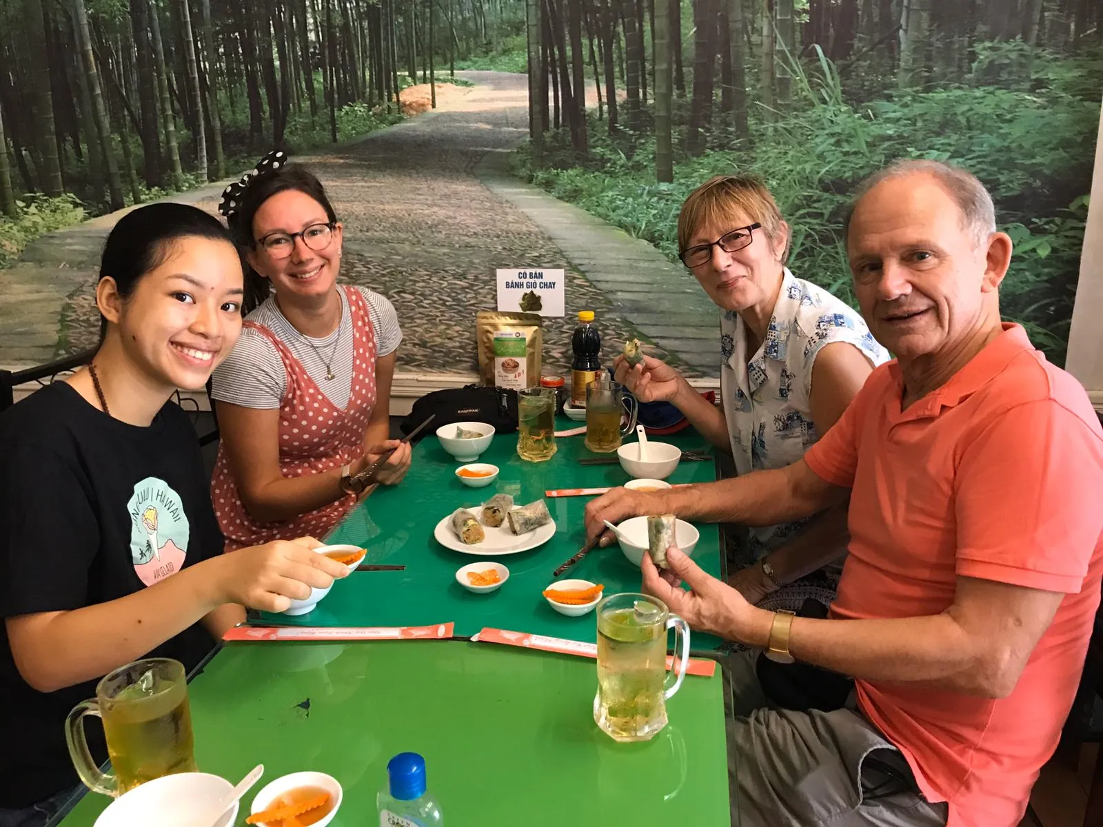 Four guests rolling spring rolls together at a green restaurant table