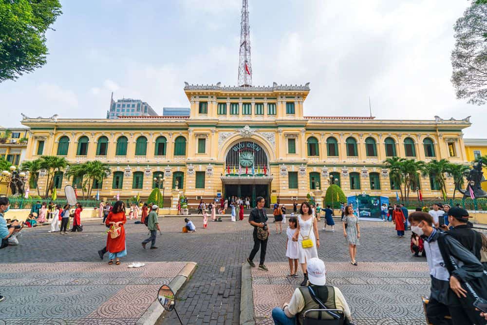 The facade of Saigon Central Post Office on a grey overcast day, people walking in front